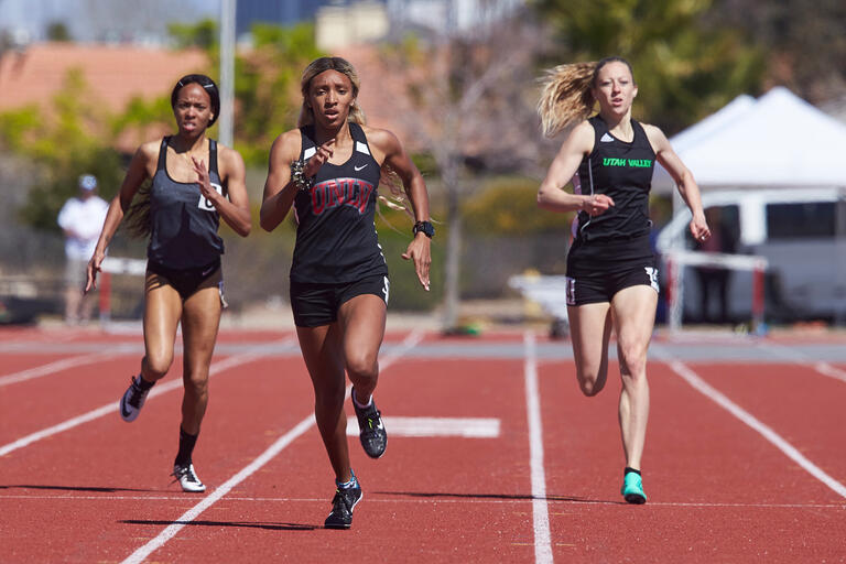 Three runners race down their lanes at a track meet.