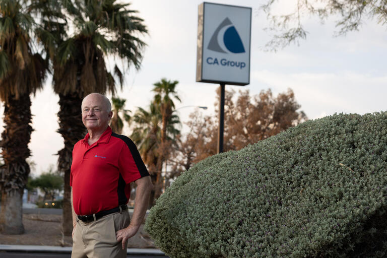 A man stands in front of a sign for the CA Group