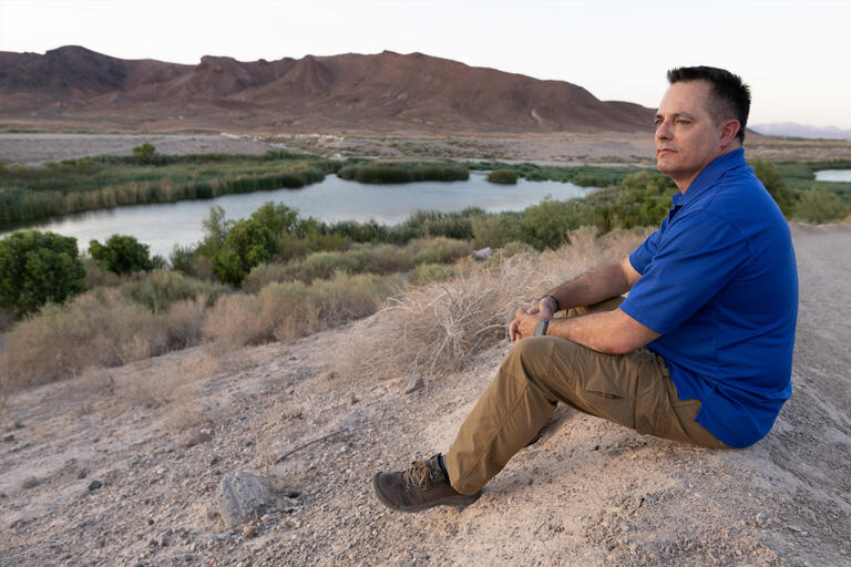 A man sits on a hill near a stream