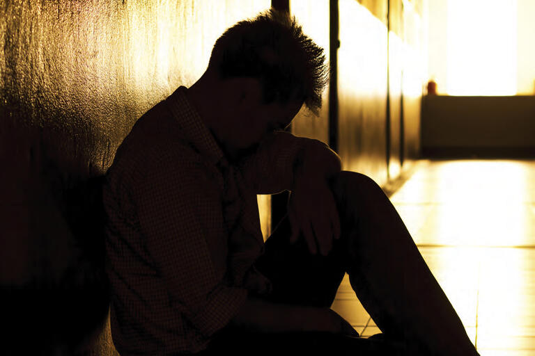 teenage male, sitting in a dark hallway, holds his head in his hands