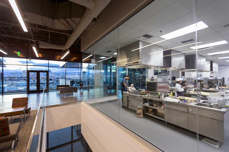 Students work in a test kitchen in front of a floor-to-ceiling windows with a view of Las Vegas at dusk.