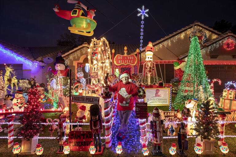man standing outside house decorated with lights and holiday figures
