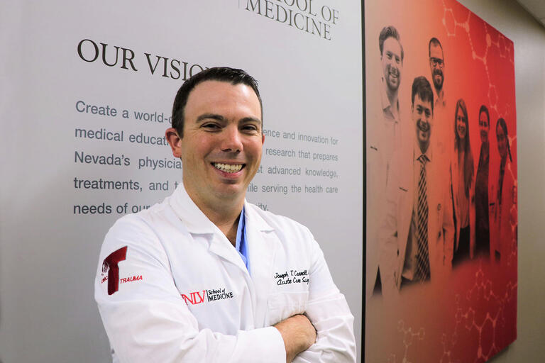 Dr. John Carroll stands with arms folded in front of a sign.
