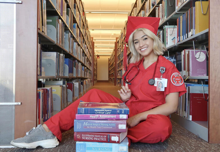 maricel gomez wears red nursing scrubs as she sits on the library floor surrounded by books