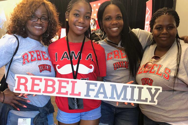 Four family members take a photo holding a sign that says Rebel Family in red and gray.