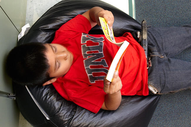 Top view angle of a young kid laying in a bean bag and reading a  book.