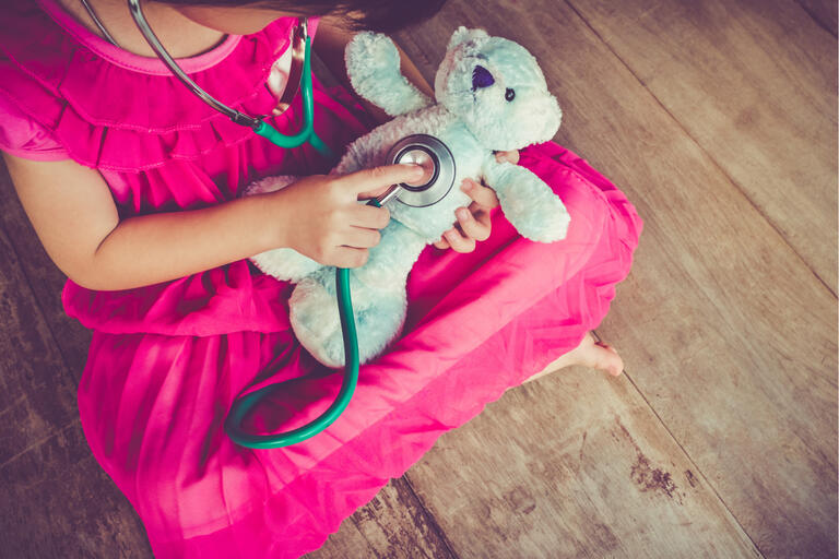 A girl holds a stethoscope to a teddy bear