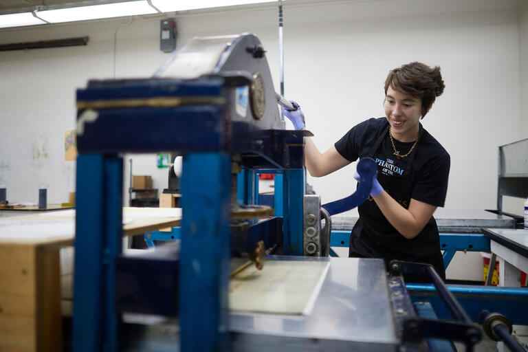 A student uses printing equipment in an art studio.