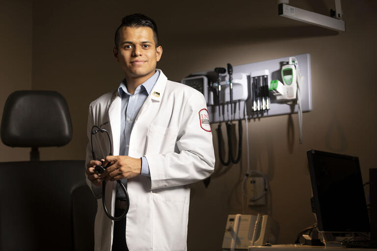 Student in white medical coat stands in front of medical equipment