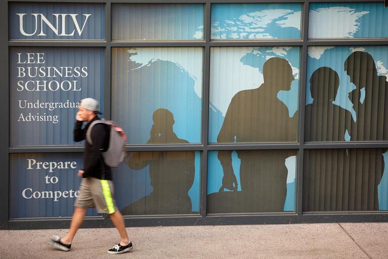 Student walking in front of a building with Lee Business School sign on the windows.