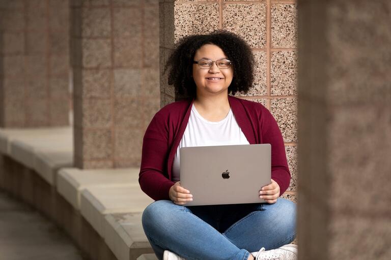 Angela Williams, a fellow with the Nevada Institute for Teacher and Educator Preparation (NITEP) at UNLV, sitting on a stone bench with a laptop open across her lap