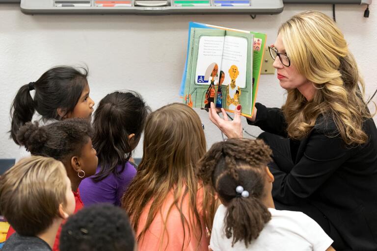 Women reading a book to a group of elementary students.