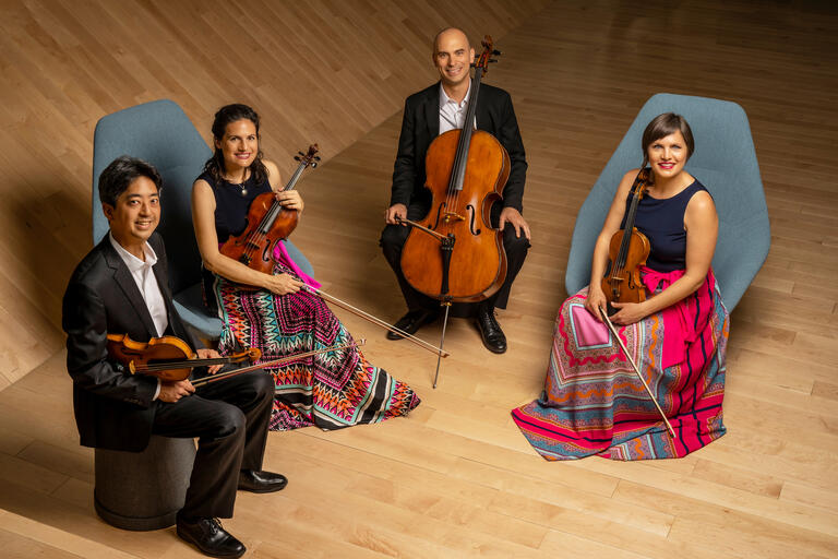 The artists in the Jupiter String Quartet, holding their instruments and sitting on a stage, look toward the camera in this promotional photo.