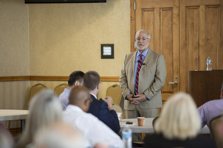 Man standing in a suit in front of lecture room.