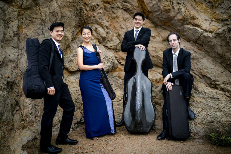 quartet posing outdoors with instrument cases