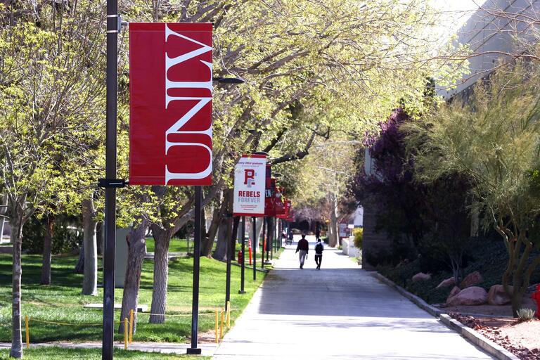 A red &quot;UNLV&quot; sign is surrounded by budding green trees.