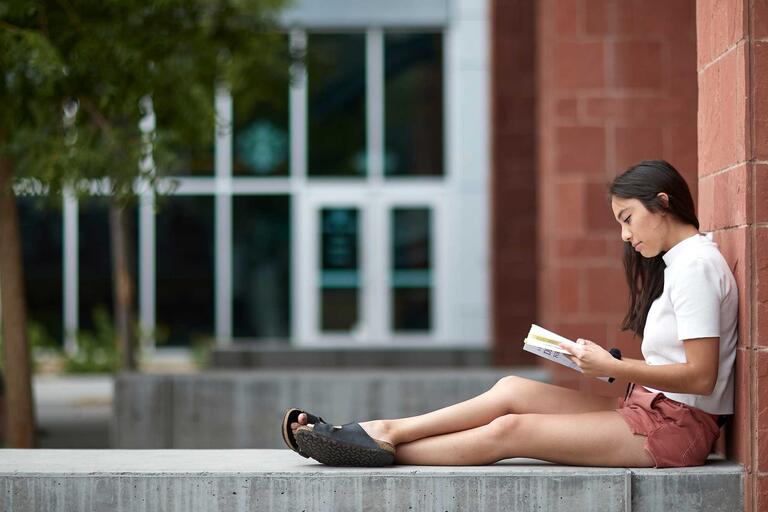 A student reads a book in front of a building
