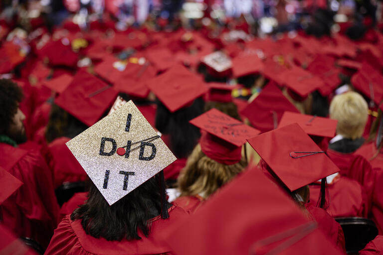 Silver graduation cap reads "I did it" among other red graduation caps.
