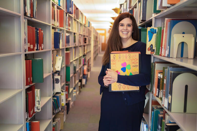 woman poses between rows of books in library