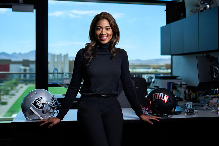 poised young woman stands in front of desk that has Las Vegas' Raiders paraphernalia on it