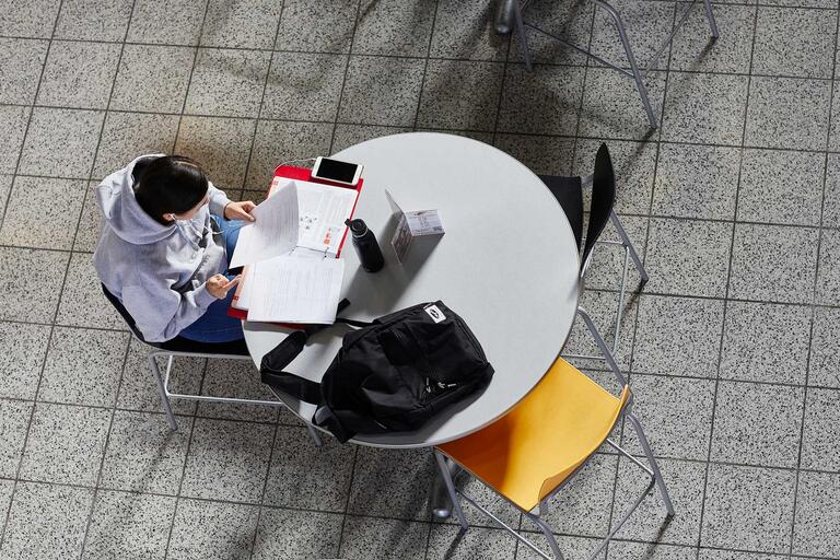 A student studies at a round table with notebooks and a computer.