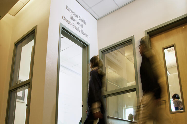 two students walking into a study room with a dedication sign on the doorway