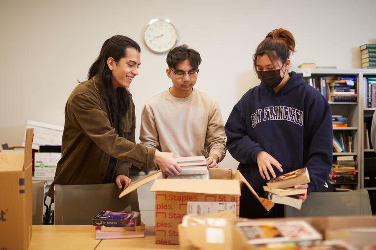 Three students putting books into a box.
