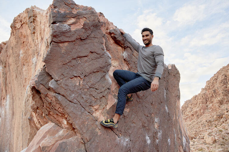 man with climbing gear poses on rock cliff