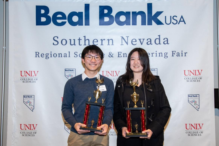 two college students pose with award plaques