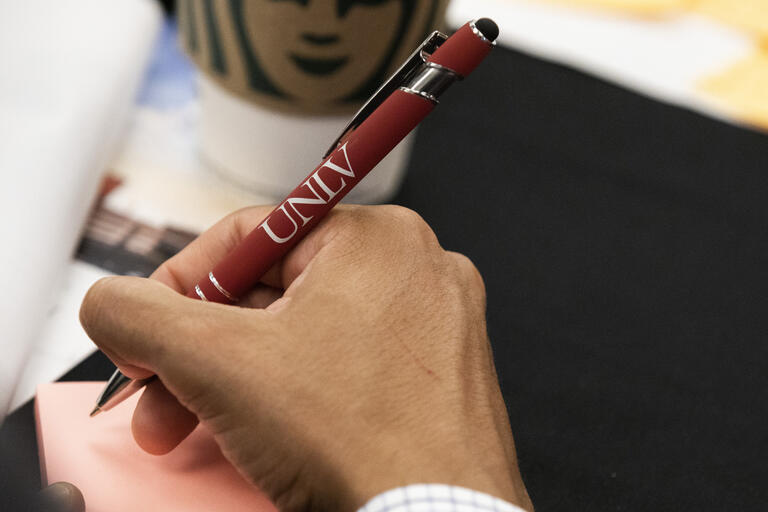 person writing on note pad with UNLV logo pen