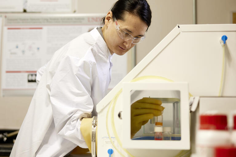man in lab coat and goggles placing a tube into equipment