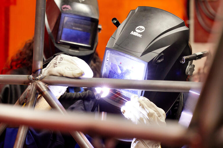two people with welding masks working on the frame of a car