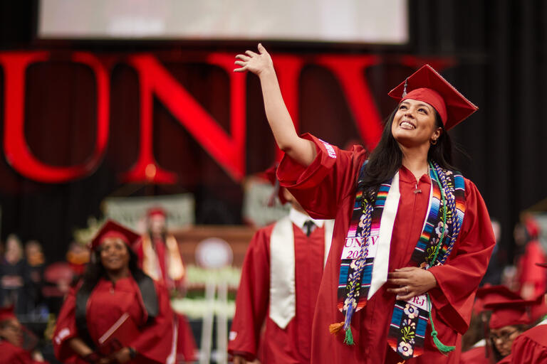 smiling and waving female in red graduation gown walks across stage
