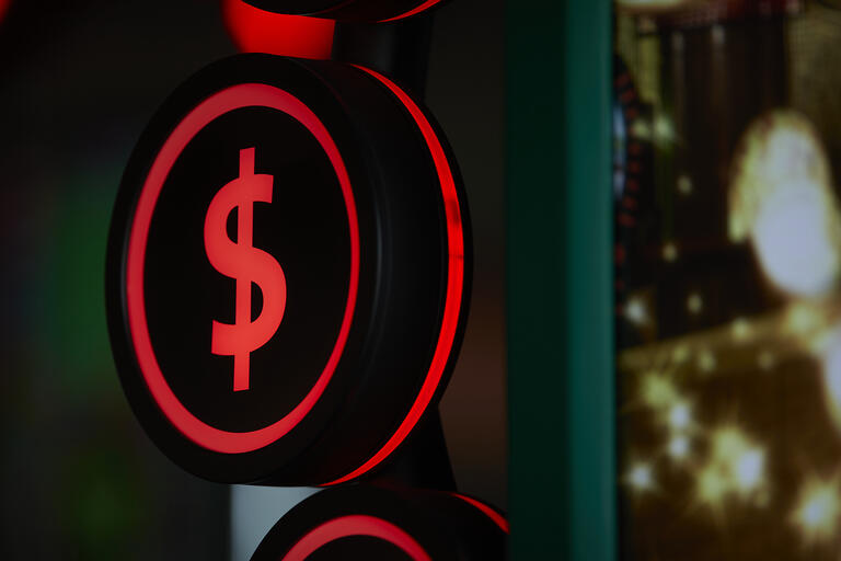 A lit up sign with a red dollar sign against a black background.