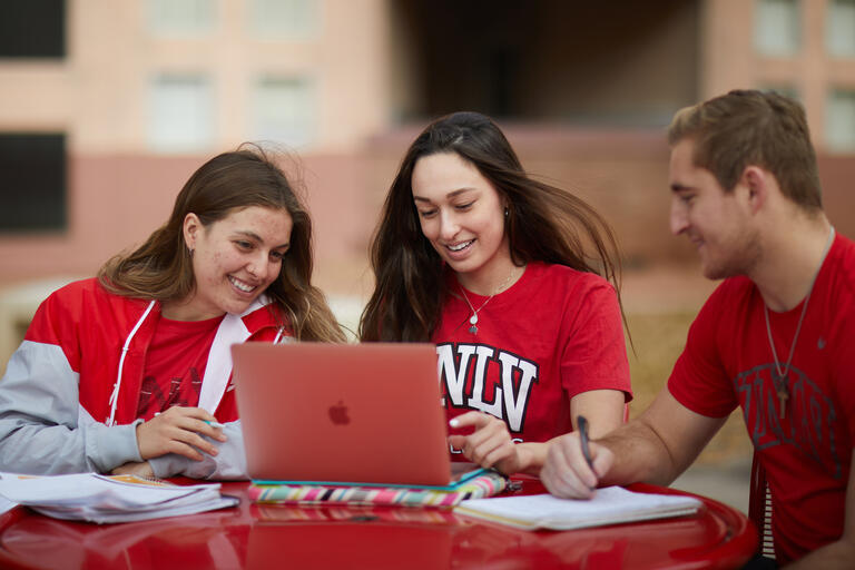 three college students at table working on laptop