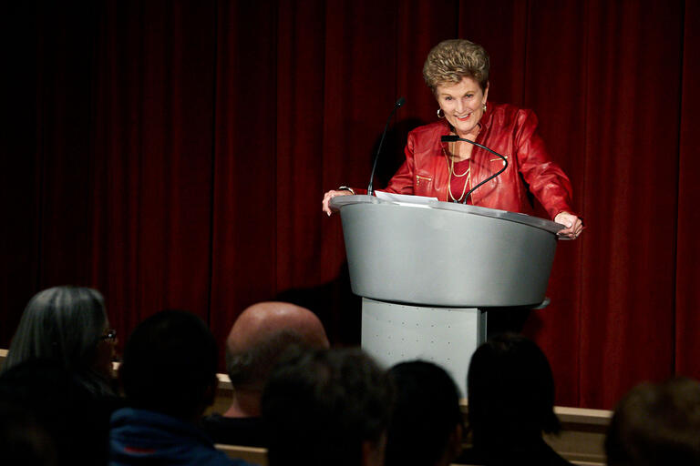 woman in red suit presenting at podium