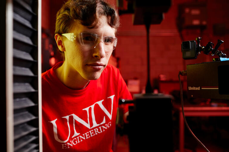 A student wearing a red UNLV Engineering shirt testing a the strength of a 3d printed piece of material.