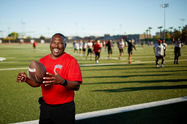 man in red shirt holding football with players in background