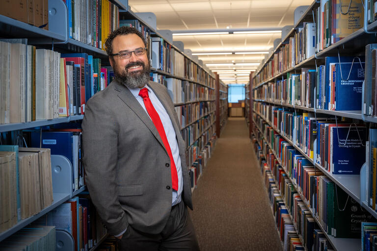 man in library standing between a row of book shelves