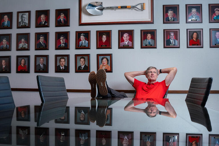 man sitting on chair with feet on table and framed photographs behind him