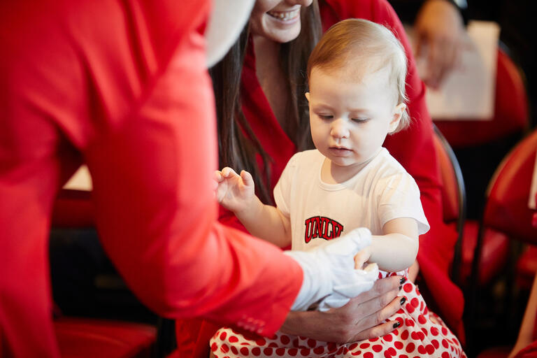 A young child in a UNLV onesie having their hand inspected.