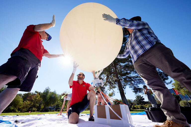 three individuals inflating a balloon for a scientific project
