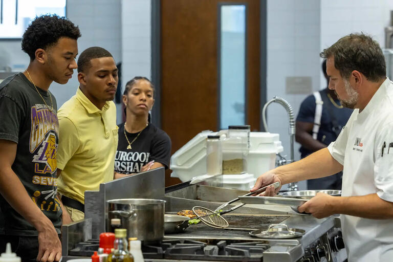three student observing a chef in a demonstration kitchen
