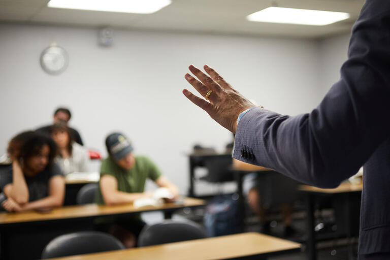 instructor's hand gesturing to class of students