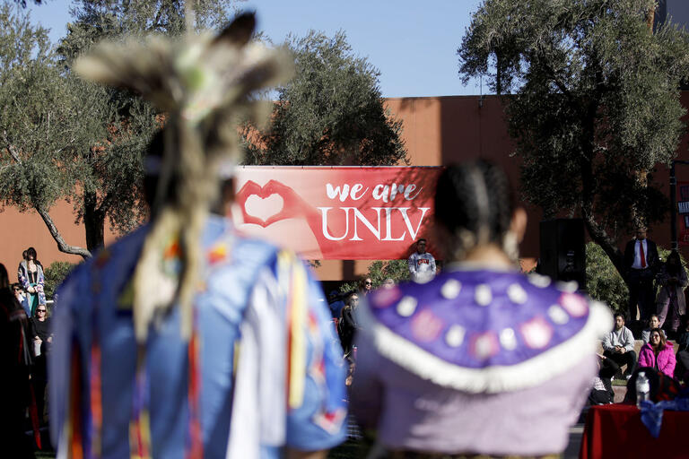 two tribal dancers facing a crowd at outdoor amphitheater with sign saying &quot;We Are UNLV&quot;