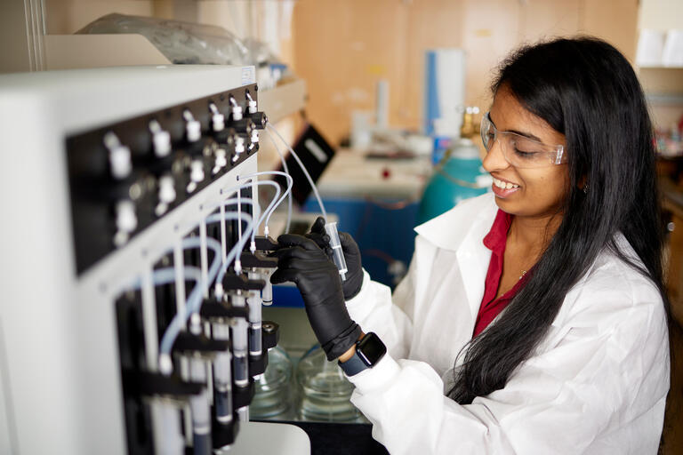 female student in labcoat working with lab equipment