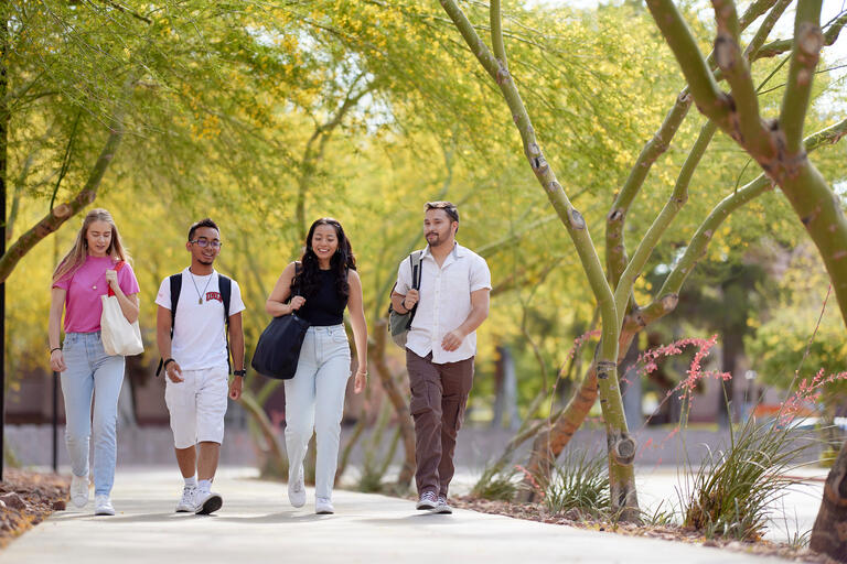 group of four students walking on a campus sidewalk