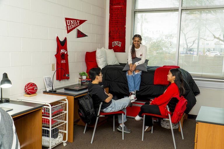 Three people talking around a bed in a dorm room