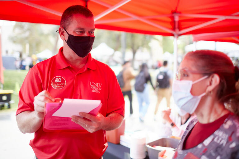 Dean of the School of Public Health in a mask talking to another colleague in a mask.
