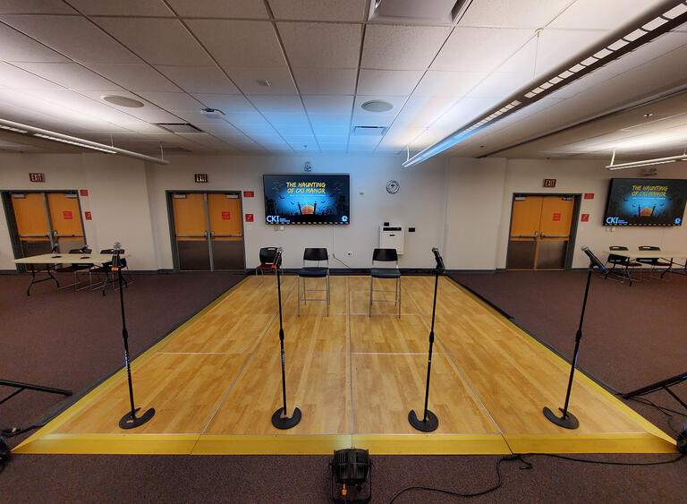 A room with a stage with four microphones and two chairs set up